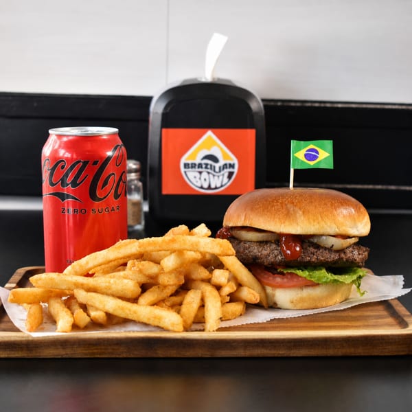 Brazilian Bowl hamburger with a flag, fries, and a Coca-Cola Zero Sugar on a wooden tray.