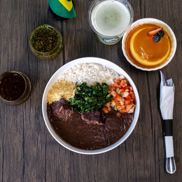 Brazilian feijoada with rice, kale, salsa, farofa, and two sauces, alongside a drink and flan.