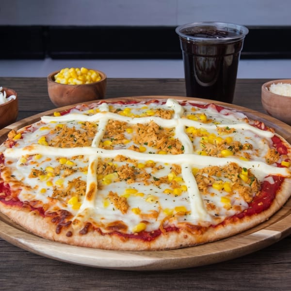 Chicken and corn pizza with a mayonnaise drizzle, served on a wooden tray with sides.