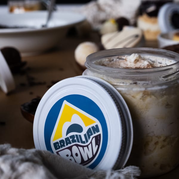 A Brazilian Bowl dessert jar with its lid open, surrounded by other desserts and a white cloth.