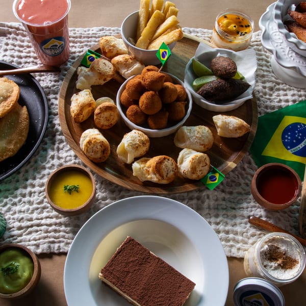 A feast of Brazilian dishes including pastries, fried snacks, desserts, and drinks, with a Brazilian flag.