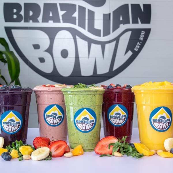 Six colorful Brazilian Bowl smoothies with fresh fruit and nuts on a white table.